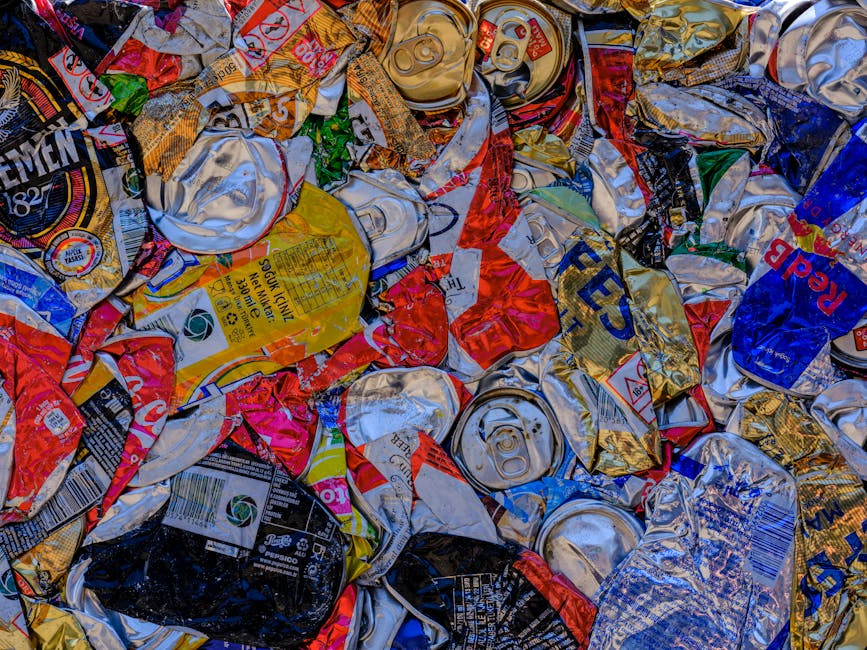 A collection of various cardboard boxes and paper waste piled on top of recycling containers outdoors, positioned against a white corrugated metal wall with a blue sign reading 'RECYCLING ONLY' featur