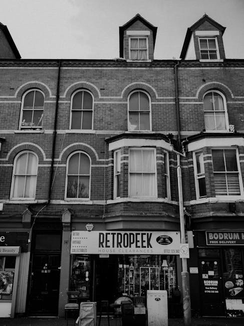 A row of Victorian-style terraced houses with ornate white ironwork balconies and decorative gable heads, positioned along a paved residential street. The buildings have brick facades with large sash 